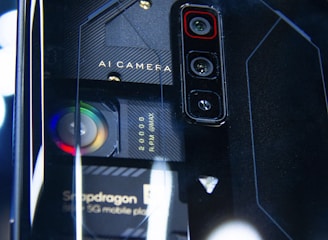 A close-up view of a smartphone's back panel showcasing its triple camera setup and other technical components. The text 'AI Camera' and 'Snapdragon' can be seen on the phone, along with visible lenses and intricate design patterns in a futuristic style.