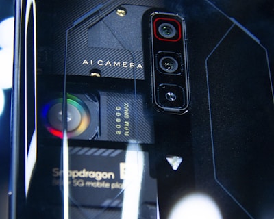 A close-up view of a smartphone's back panel showcasing its triple camera setup and other technical components. The text 'AI Camera' and 'Snapdragon' can be seen on the phone, along with visible lenses and intricate design patterns in a futuristic style.